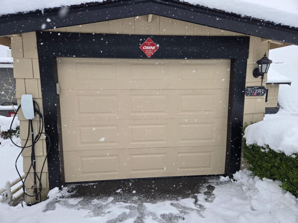 A snow-covered garage door with a beige surface and black trim