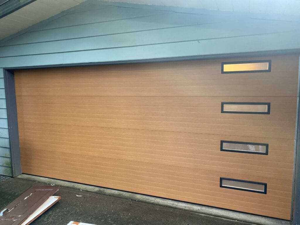 A modern, wooden garage door with three vertical windows, set against a blue house exterior.