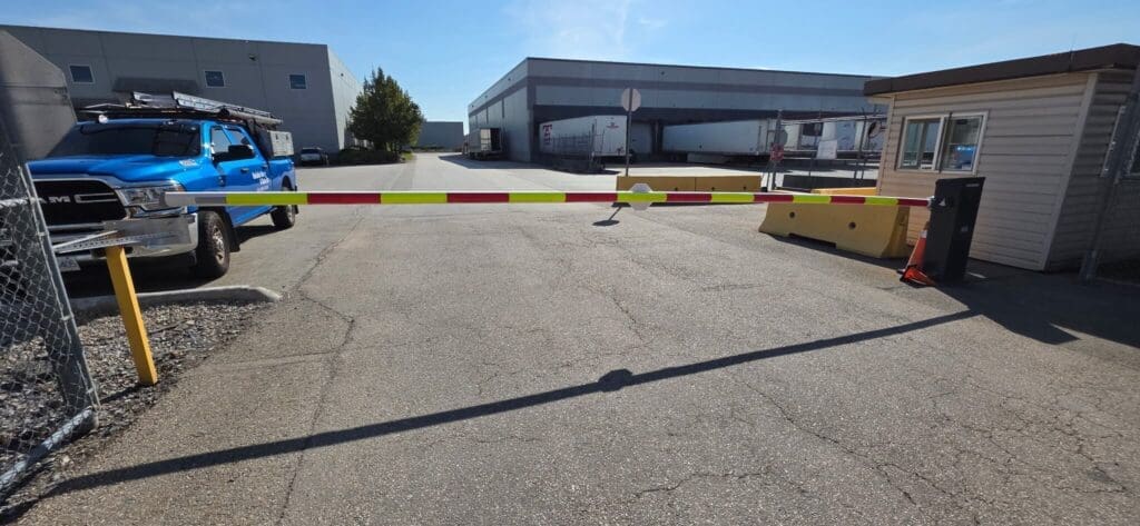 A blue pickup truck parked next to a gated entrance blocking a gravel road.