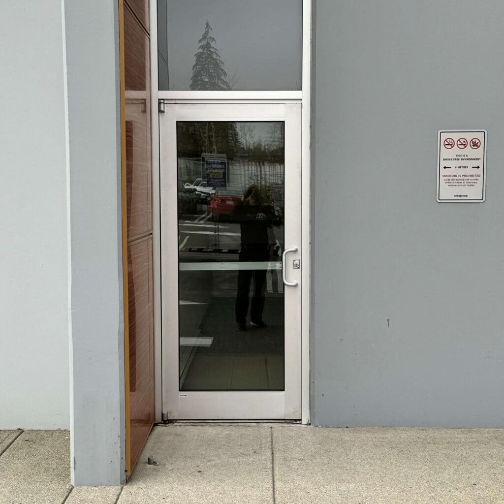 A clear glass door with a metal frame, positioned on a gray wall.