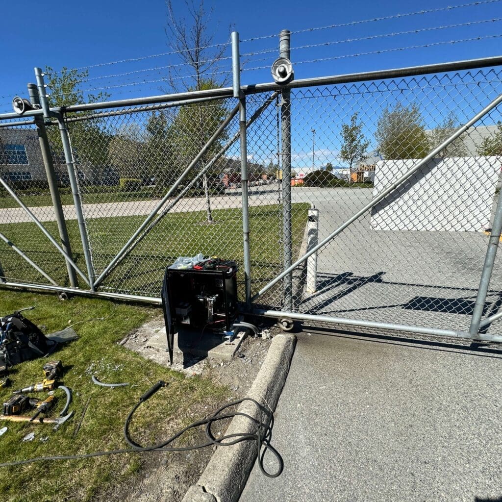 A chain-link gate partially open with a welding machine positioned nearby on a concrete surface.