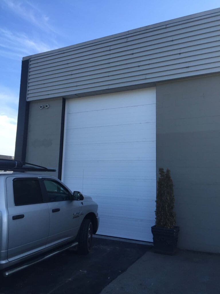 Image of a partially open garage door with a black cover, revealing equipment inside.