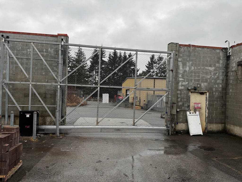 A large metal gate is closed at an industrial facility, flanked by gray concrete walls.