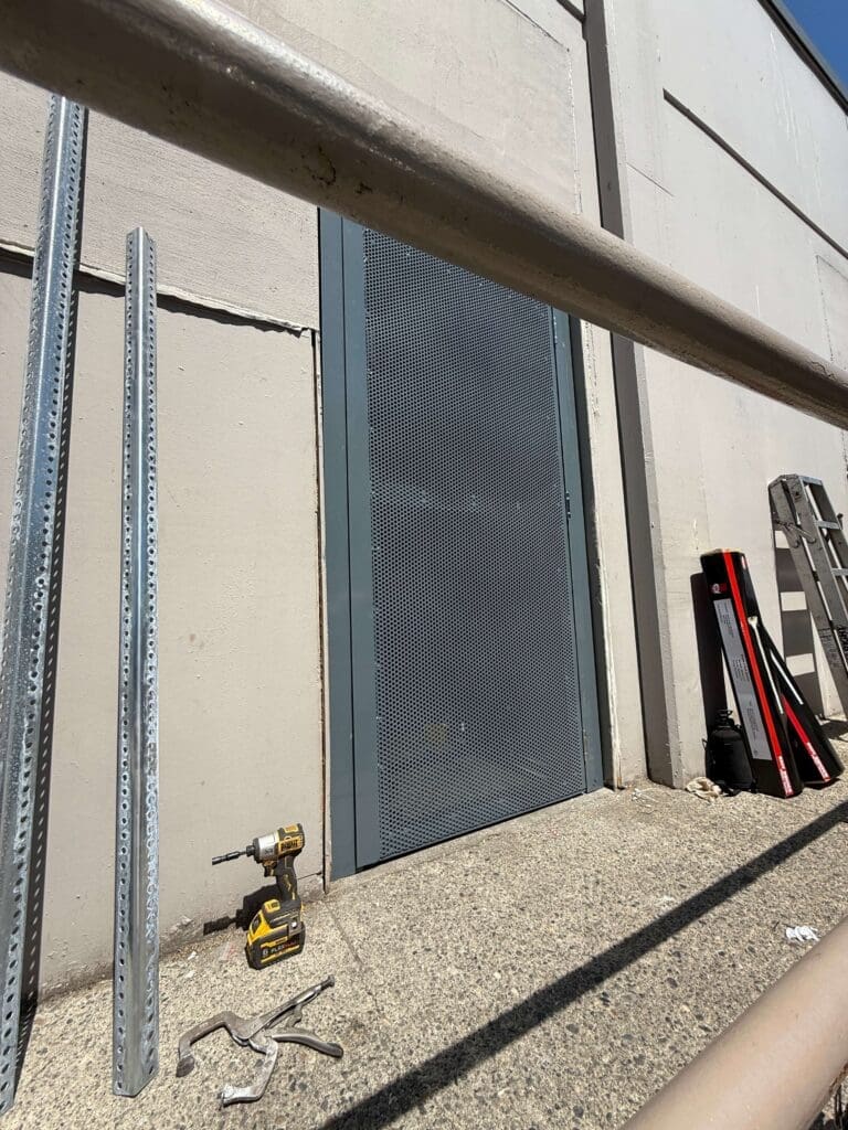 A gray door with a mesh screen is set into a light-colored wall