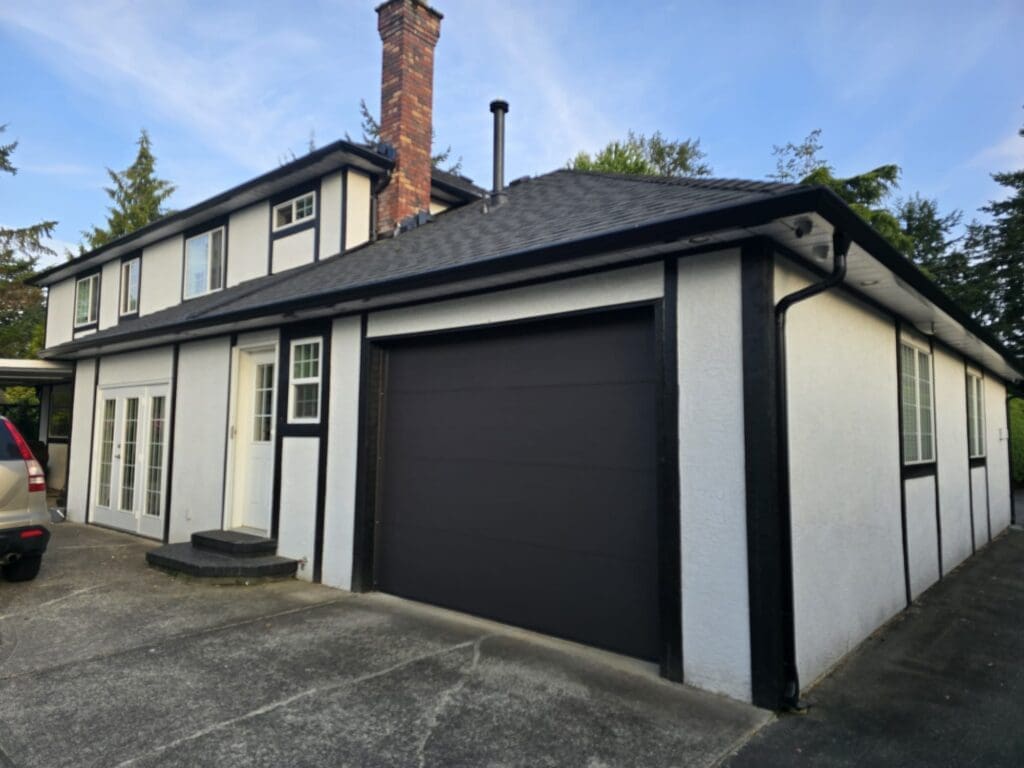A two-story house with a modern exterior, featuring a grey garage door and white walls with black trim.