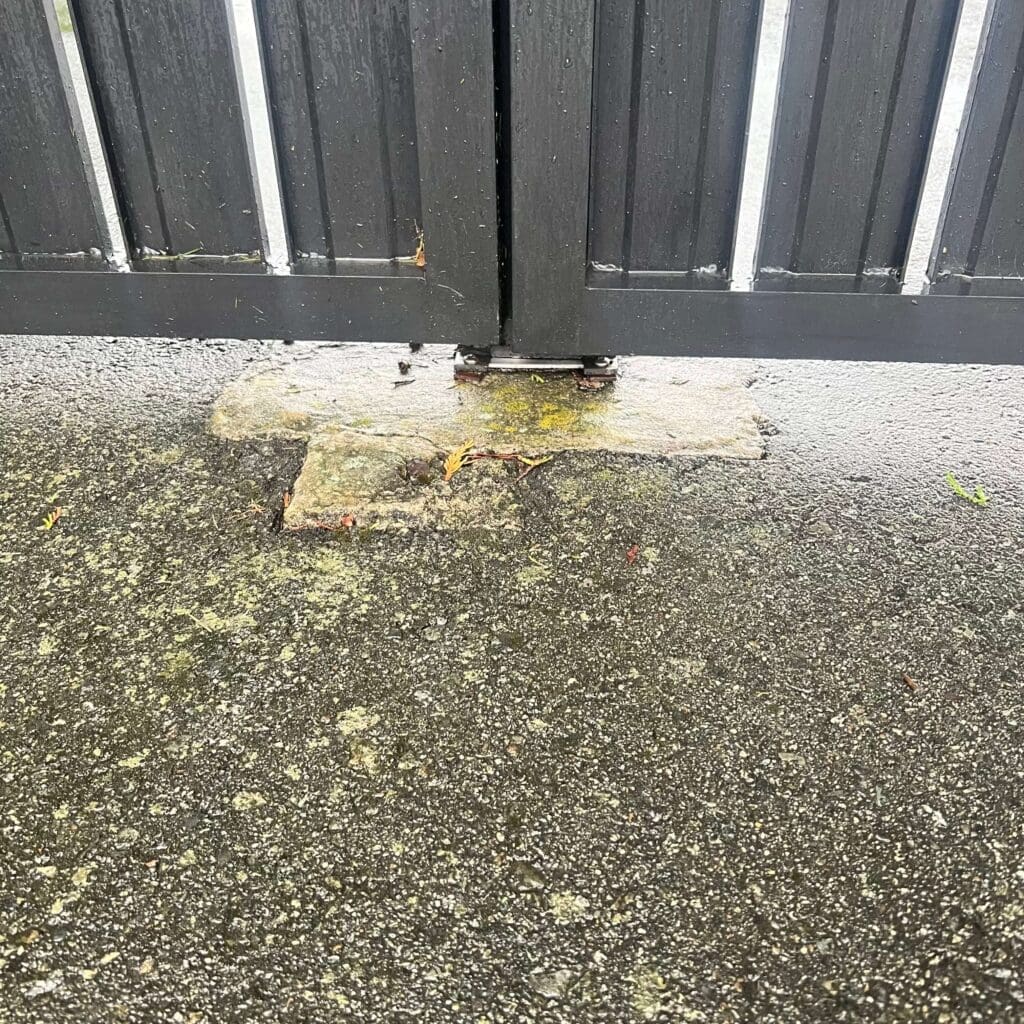 A close-up view of a black metal gate partially closed, resting on a gray stone block.