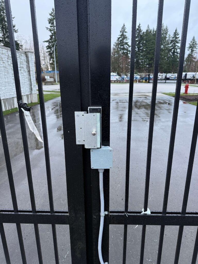 A close-up view of a metal gate latch on a black vertical gate with raindrops on it.