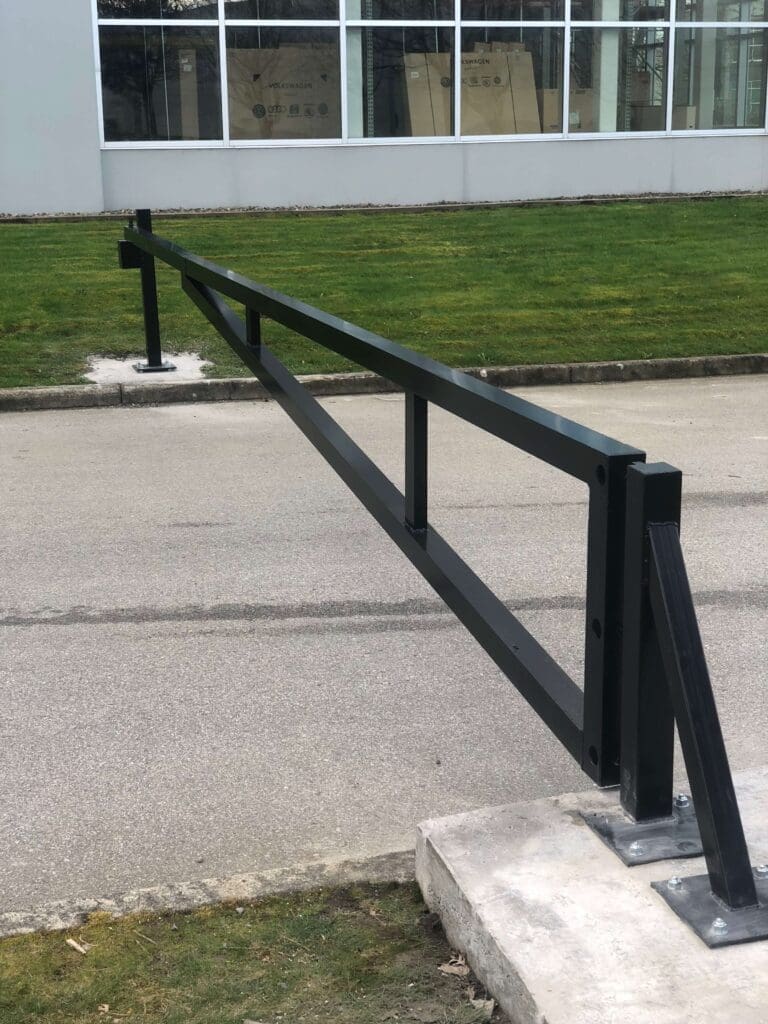A metal railing along a concrete barrier beside a grassy area.